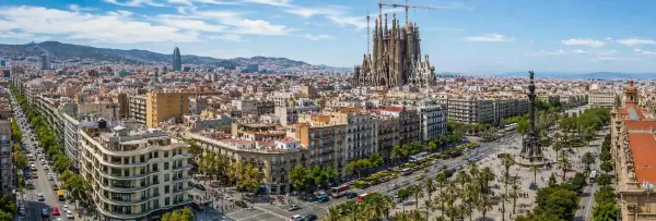 Panoramic daytime view of Barcelona featuring the Sagrada Família, modern city skyline, tree-lined avenues, and surround