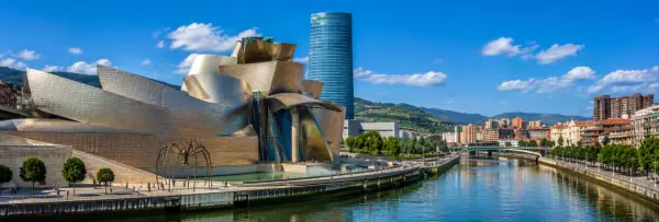 Guggenheim Museum Bilbao beside the Nervión River with the city and green hills in the background