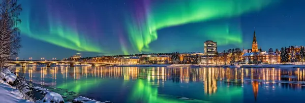 Umeå, Sweden, glowing northern lights over a snowy riverside city at night