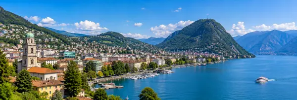 Lugano, Switzerland with Lake Lugano, waterfront buildings, green hills, and Alpine mountains